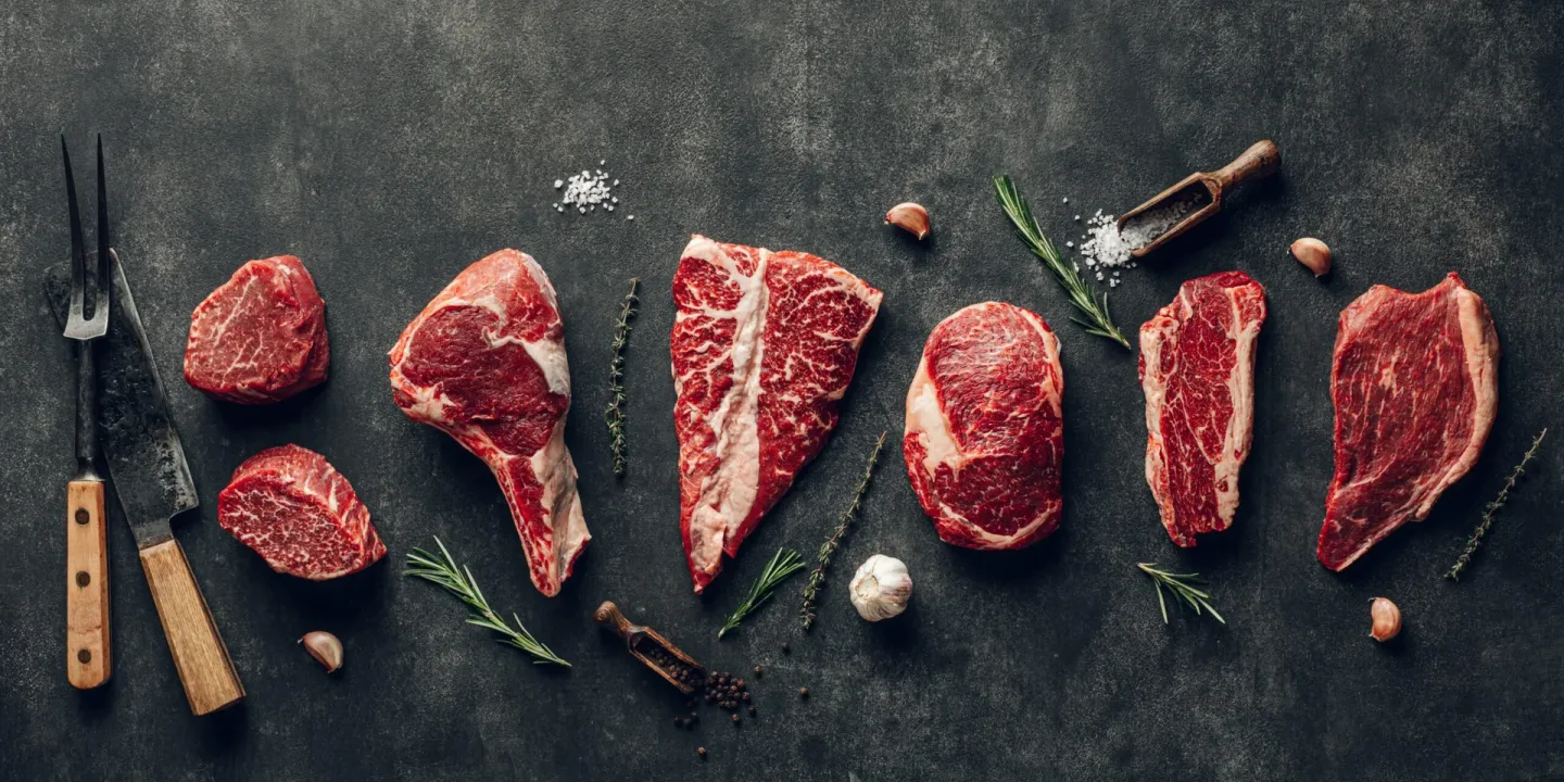 Råa köttstycken med kryddor och kniv på en mörk bänk